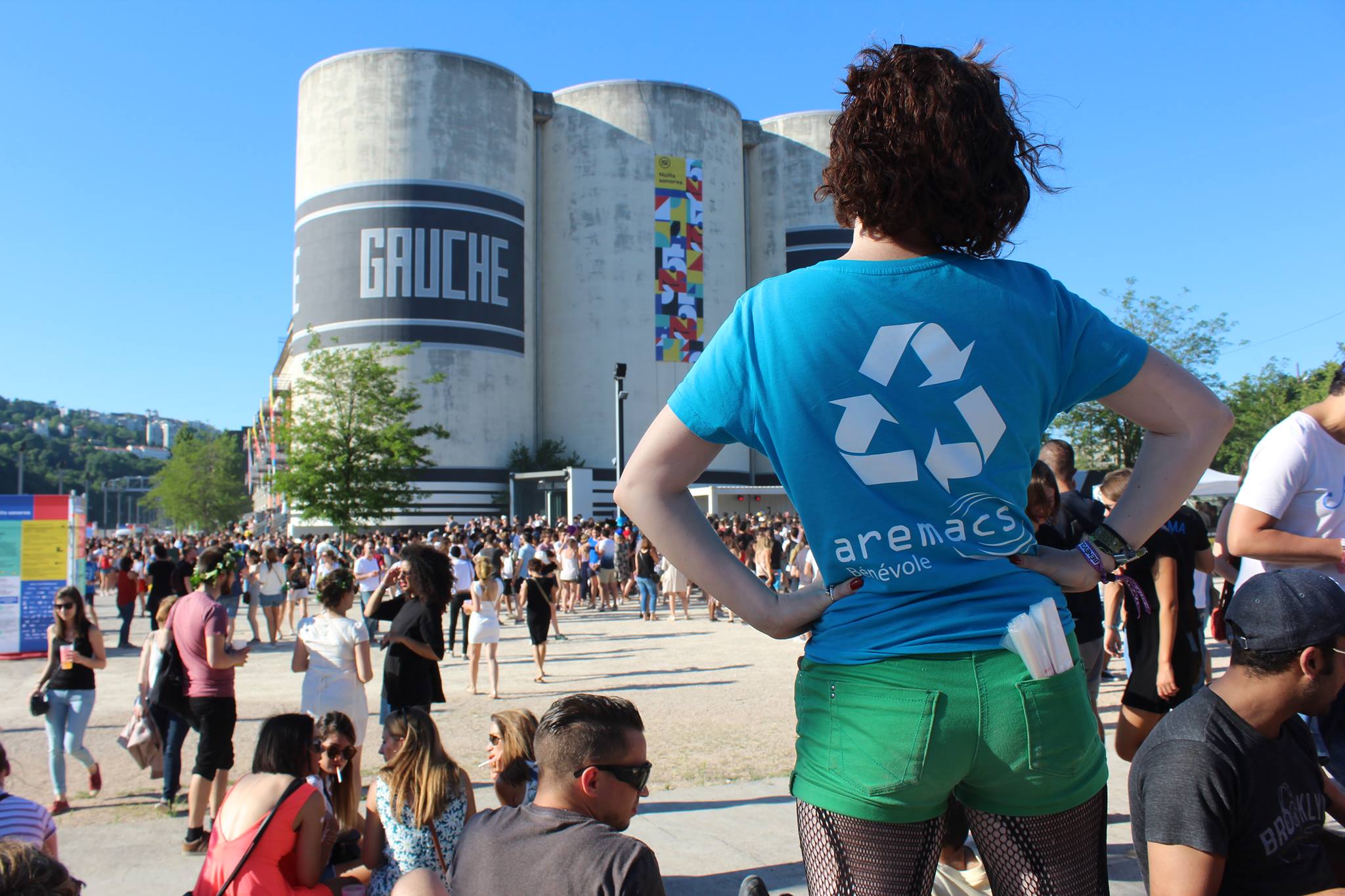 aremacs-association-lyon Une bénévole de l'association lyonnaise Aremacs se tient de dos devant la sucrière, dans le quartier de la Confluence. Elle porte le T-shirt de son association.